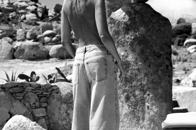 Eine Person in hellen Jeans steht vor einem großen Felsen in einer Naturumgebung.